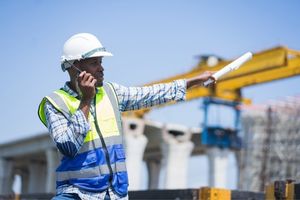 construction operative wearing hi-vis and a hardhat pointing and using a walkie talkie