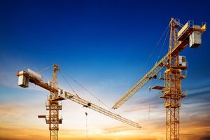 two tower cranes against the sunset on a construction site