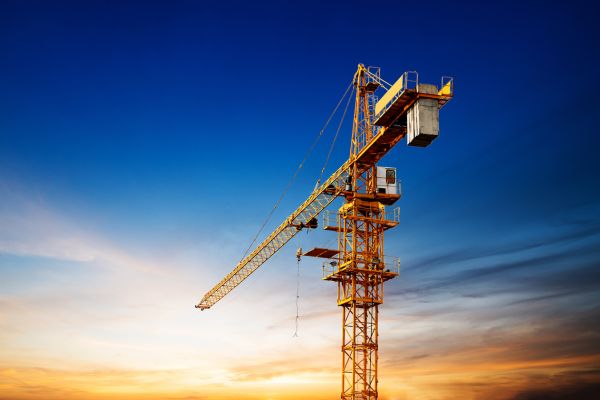 Low angle shot of a large yellow tower crane set against a vibrant evening sky